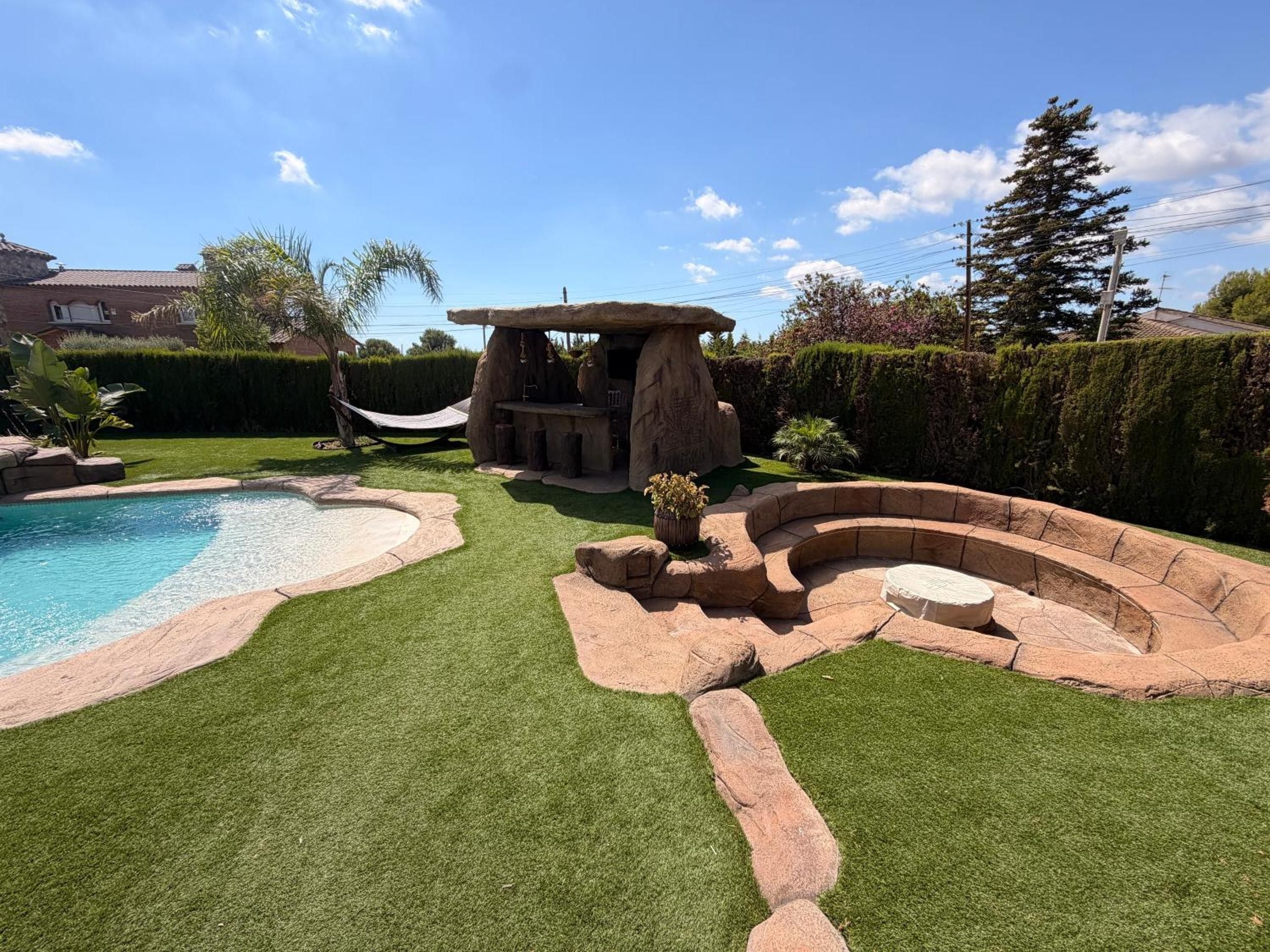 Un jardin avec une piscine, un hamac et une structure en pierre.