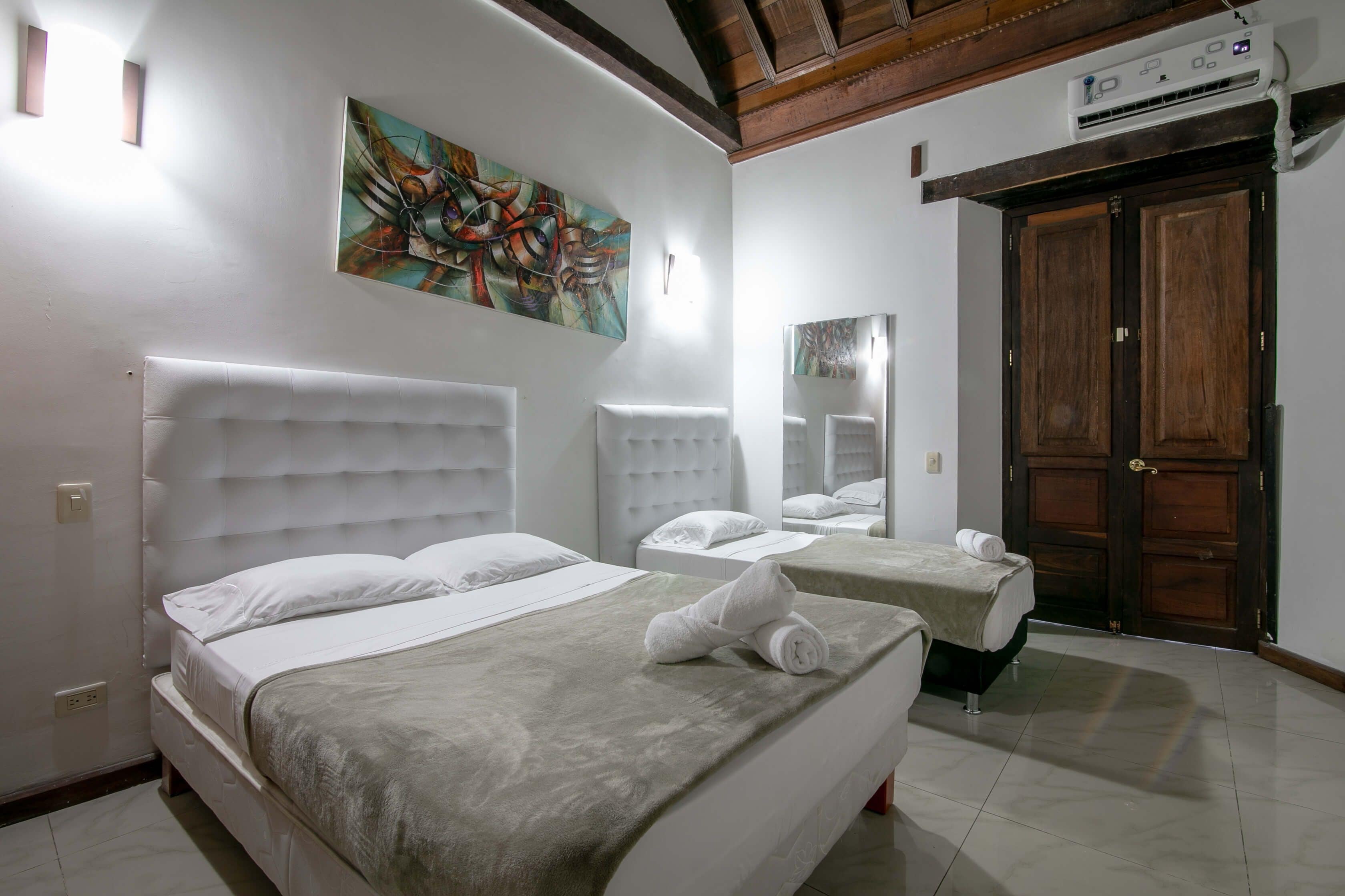 A hotel room with two beds, a large painting on the wall, and a wooden door.