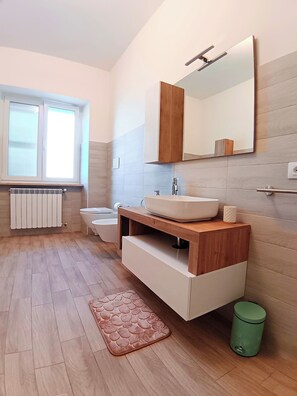 Un bagno moderno con un mobile bagno in legno, uno specchio grande, un water e un termosifone.