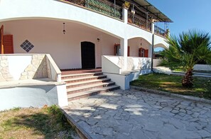 Un edificio con una scala in pietra che conduce a una porta nera, un balcone coperto con ringhiere in metallo e una palma sullo sfondo.