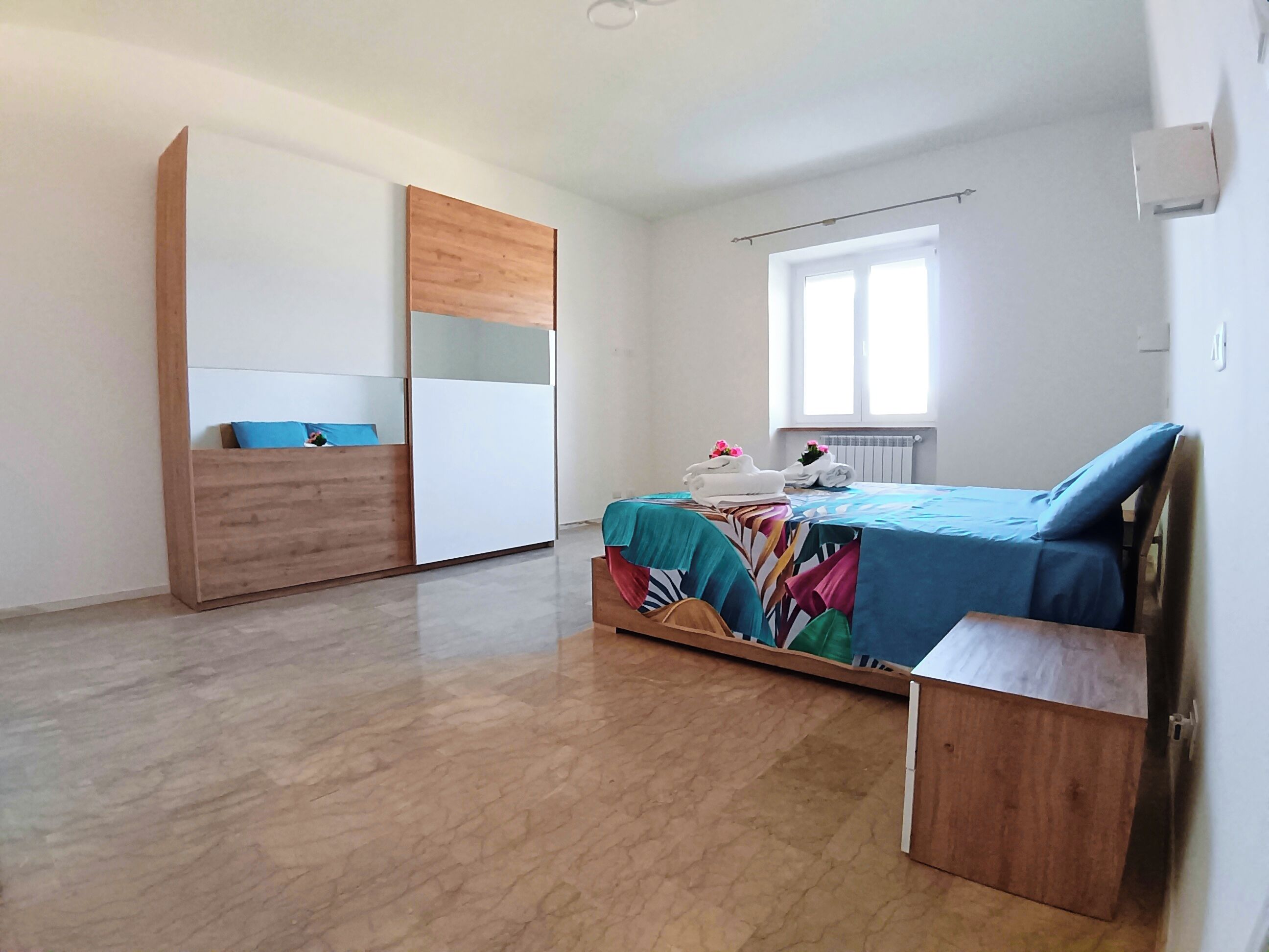 Un dormitorio con cama, armario, ventana y radiador.