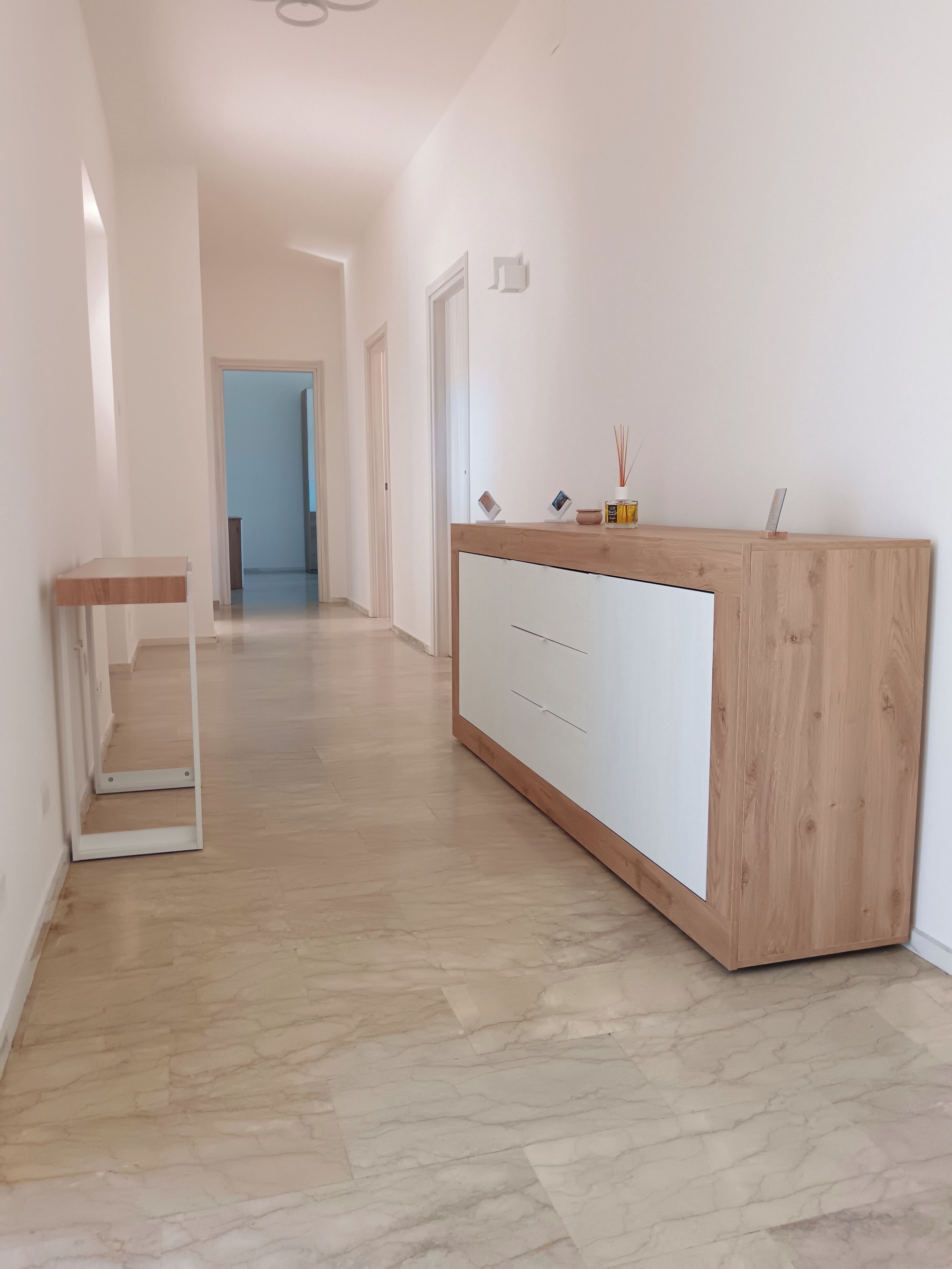 A hallway with a wooden reception desk, a marble floor, and a door at the end.