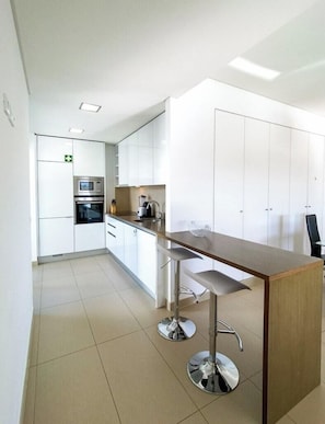 A modern kitchen with white cabinets, stainless steel appliances, and a bar area with stools. - Apartment 'Cavalo Preto' with Shared Pool, Wi-Fi and Air Conditioning (Faro)