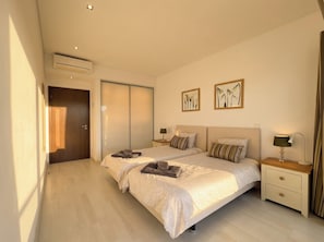 A hotel room with a double bed, two bedside tables, a nightstand, a wall-mounted air conditioner, and two framed artworks. - Apartment 'Cavalo Preto' with Shared Pool, Wi-Fi and Air Conditioning (Faro)