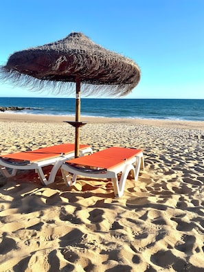 A beach with two lounge chairs and a thatched umbrella. - Apartment 'Cavalo Preto' with Shared Pool, Wi-Fi and Air Conditioning (Faro)
