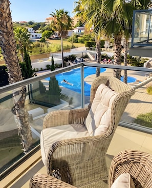 A glass-enclosed balcony with a wicker chair, a pool, and a view of a residential area. - Apartment 'Cavalo Preto' with Shared Pool, Wi-Fi and Air Conditioning (Faro)