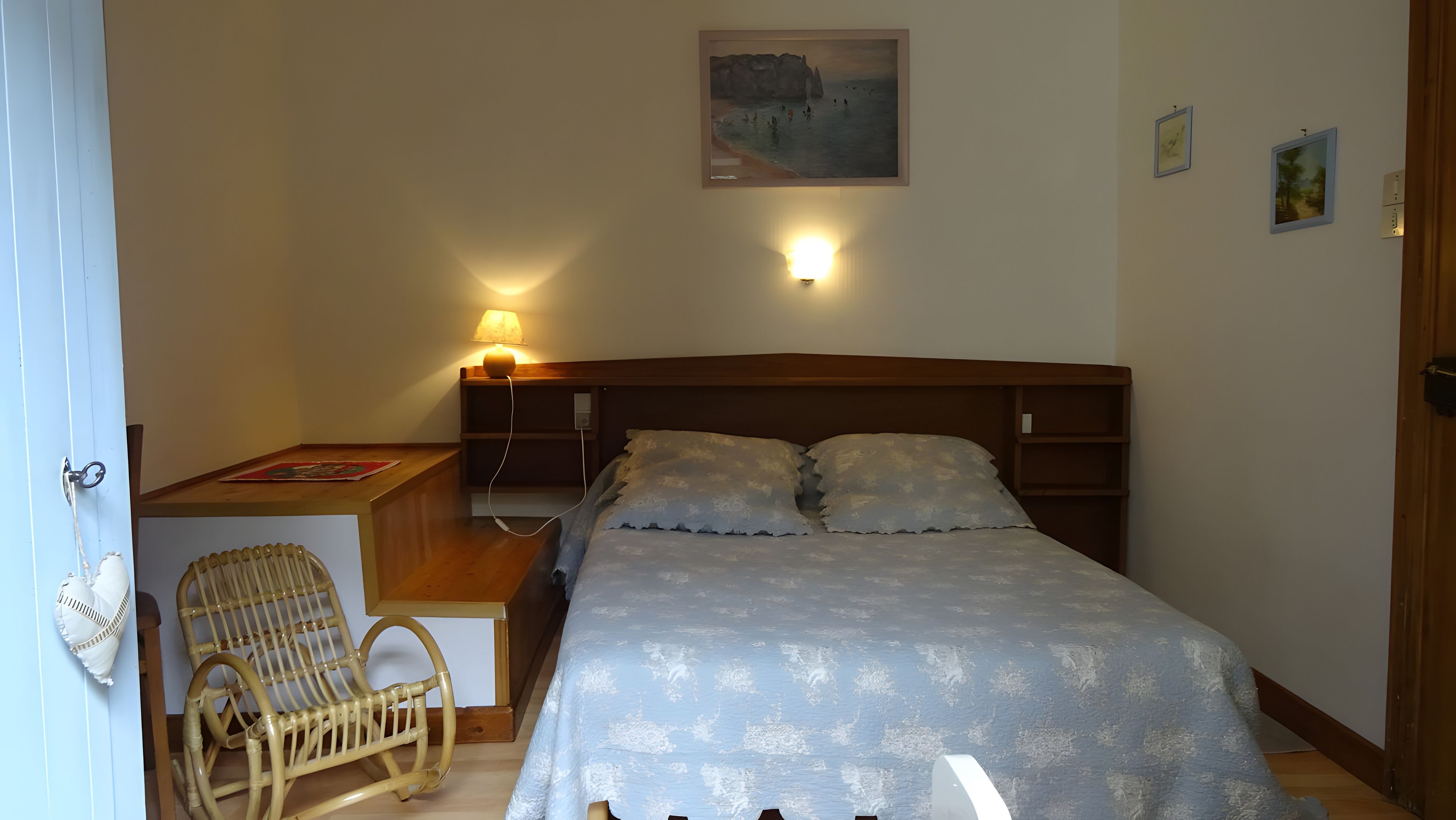 Une chambre à coucher avec un lit, une table de chevet, une lampe, une chaise et un tableau au mur.
