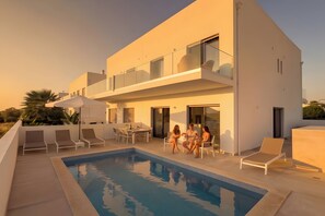 Una casa moderna de dos pisos con piscina, mobiliario exterior y un balcón.