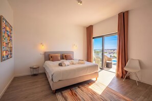 Habitació d'hotel moderna amb un llit gran, vistes a la ciutat i un balcó amb una cadira.