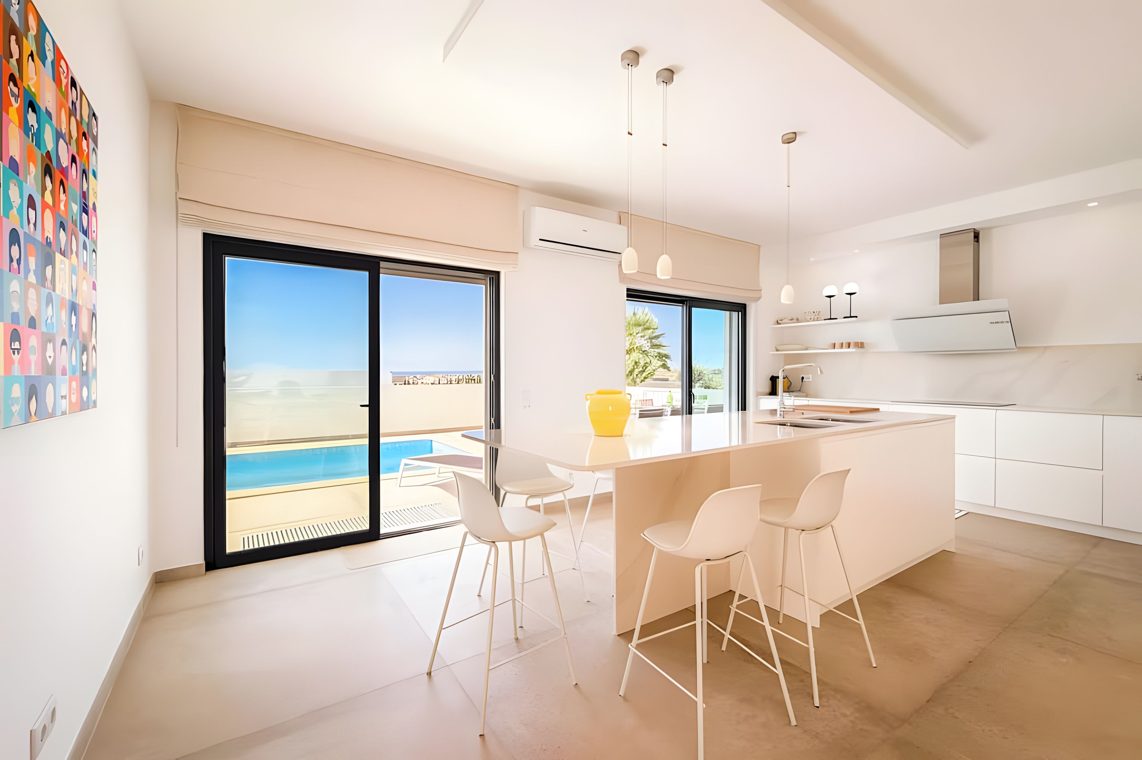 A modern kitchen with a large island, bar stools, and a view of the sea through the sliding doors.