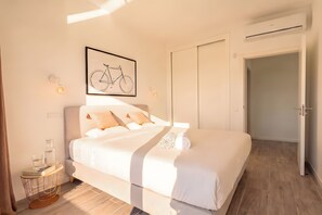 Un dormitorio moderno con una cama grande, una obra de arte con una bicicleta enmarcada, lámparas de noche y una puerta a la derecha.