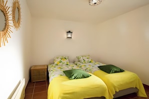 Un dormitorio con dos camas, una lámpara en la pared y un cesto de ropa.