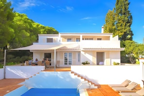 Una casa de dos pisos con piscina, mobiliario exterior y una escalera que lleva a la piscina.