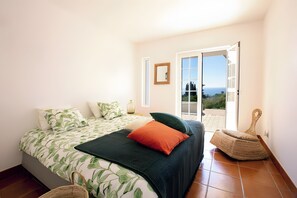 Un dormitorio con cama, almohadas, un florero y vistas al exterior a través de una puerta.