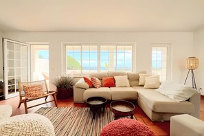 Una sala de estar con sofá, sillones, una mesa de centro y vista al mar a través de amplios ventanales.