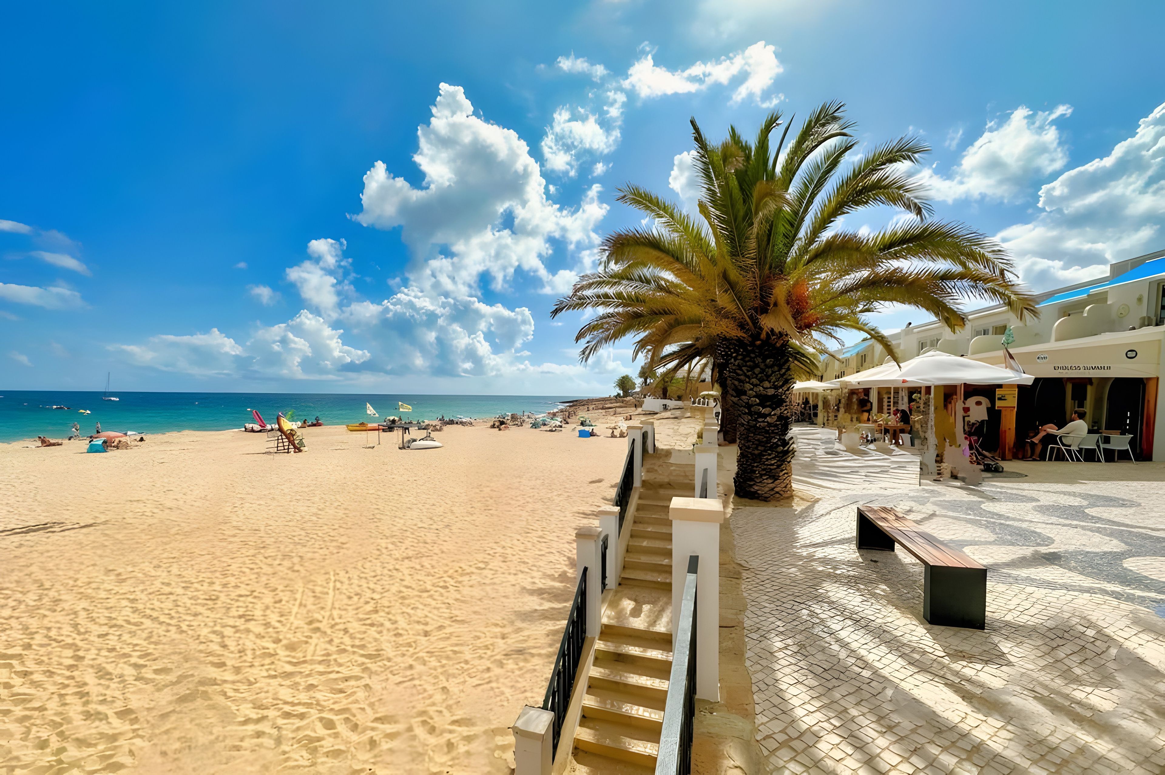 A beach with a palm tree, a staircase leading to a building, and a clear blue sky.