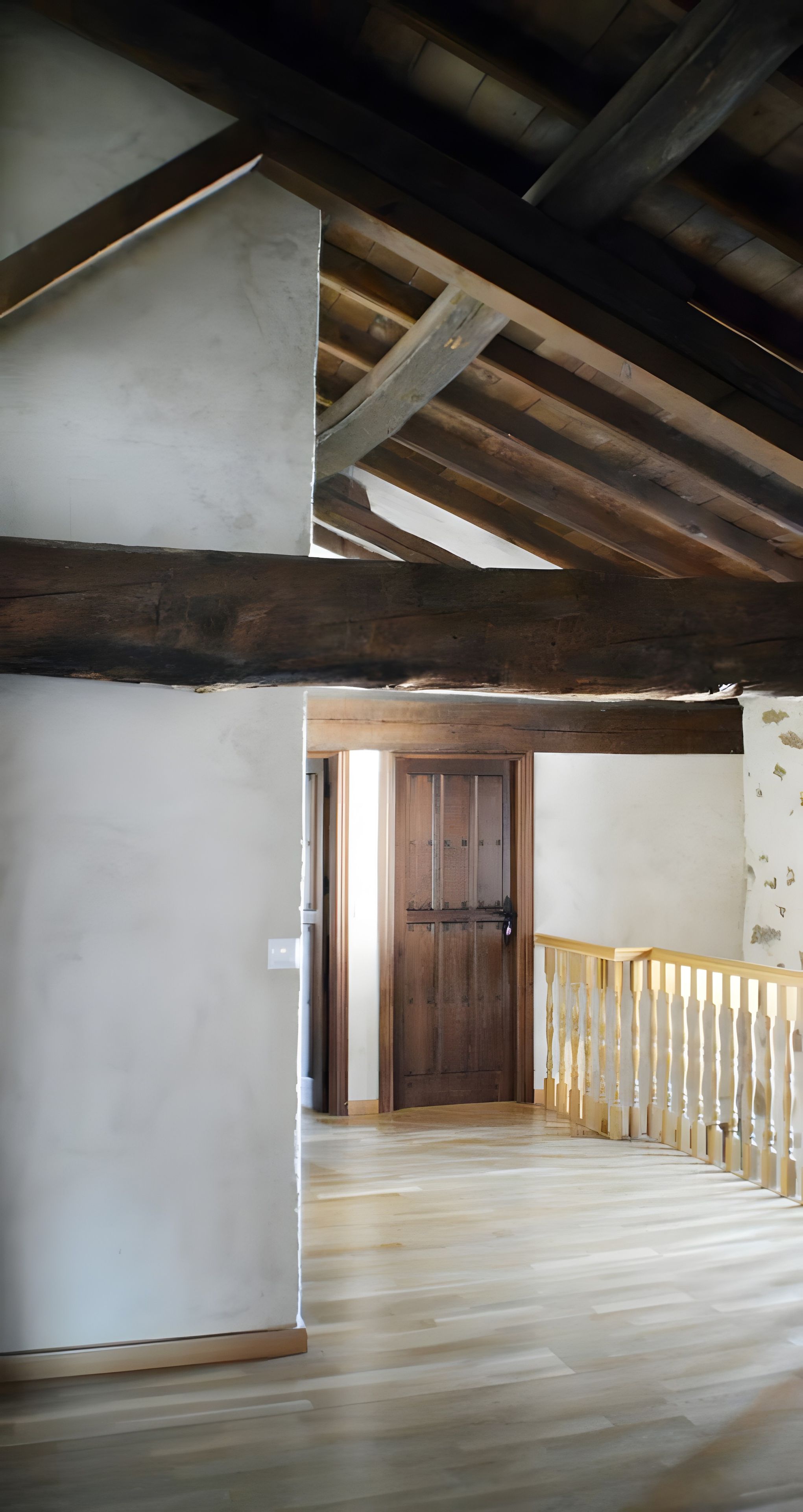 Un espacio interior con una escalera de madera, una puerta de madera y una pared blanca.