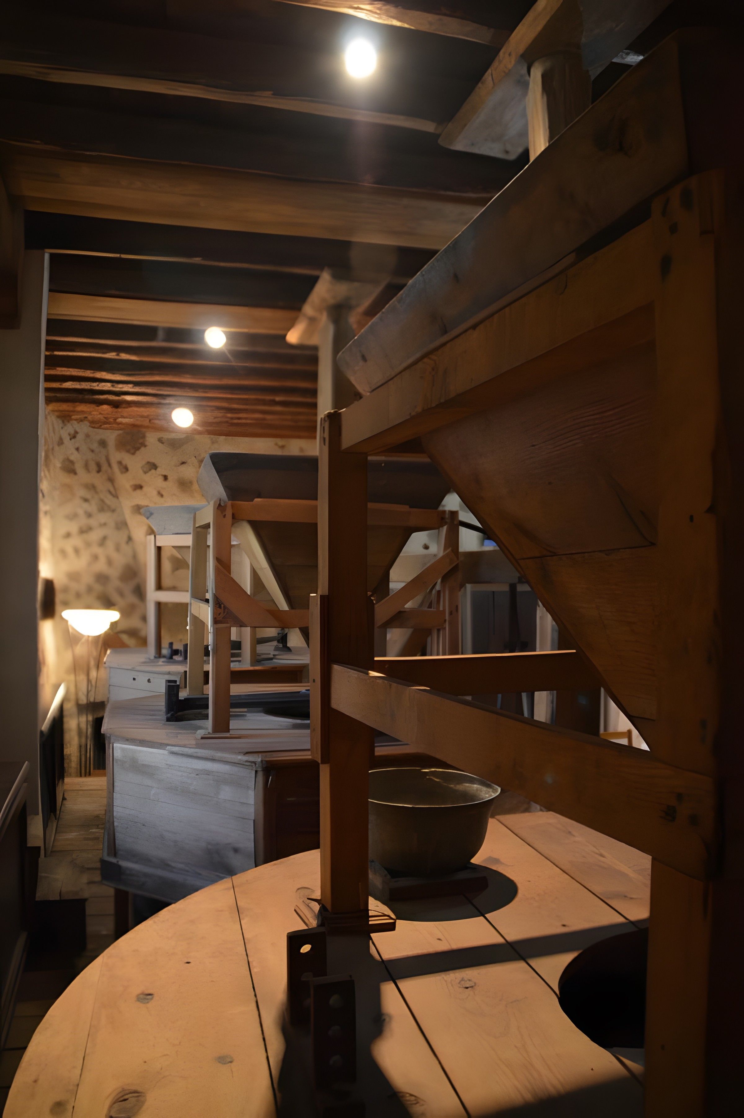Un interior de madera con una mesa central, una lámpara colgante y una escalera que lleva a un nivel superior.