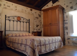 Une chambre à coucher avec un lit, une armoire en bois, un mur en pierre et une fenêtre.