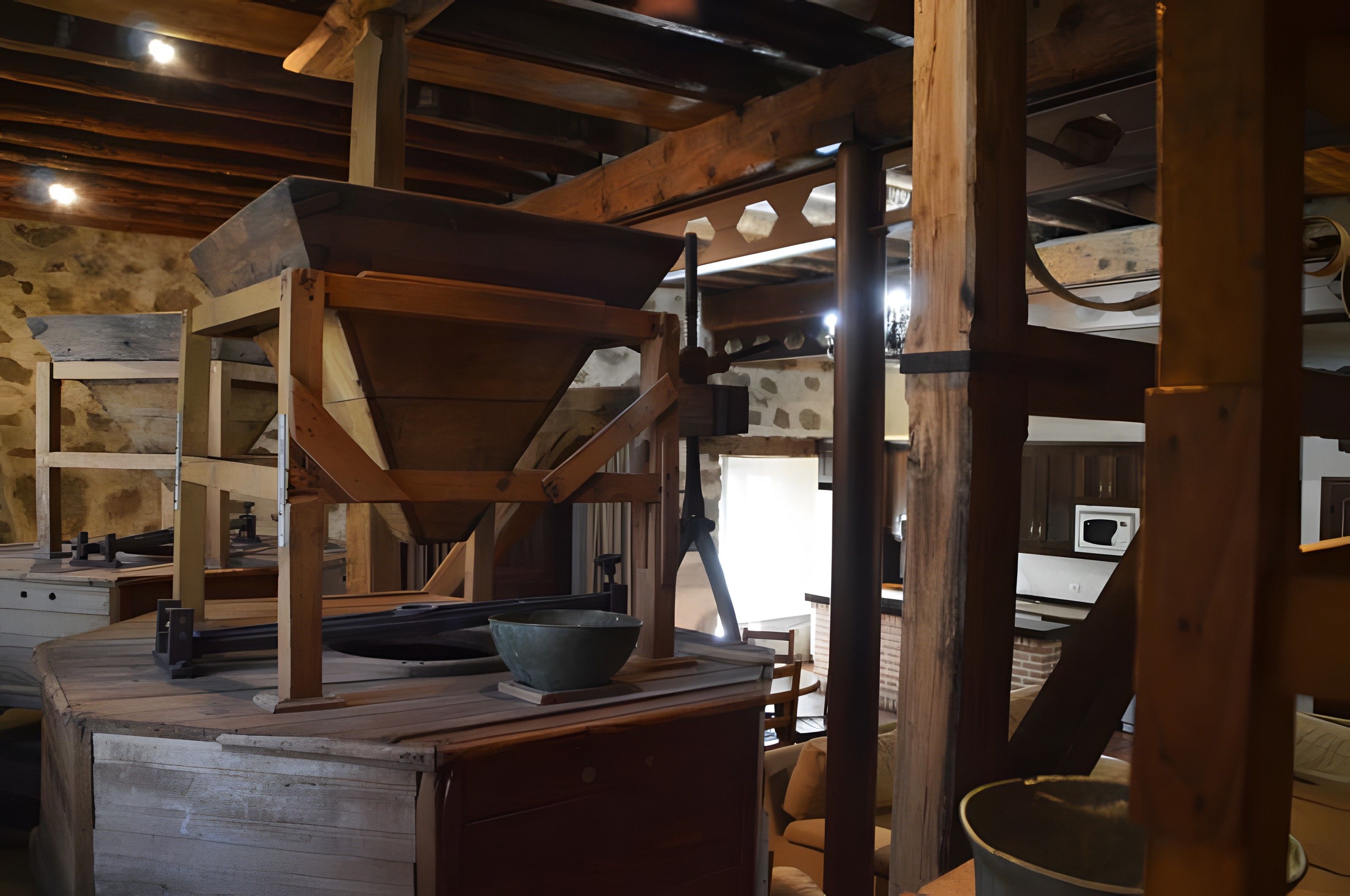 A rustic kitchen with wooden beams, a stone wall, and a large wooden table.