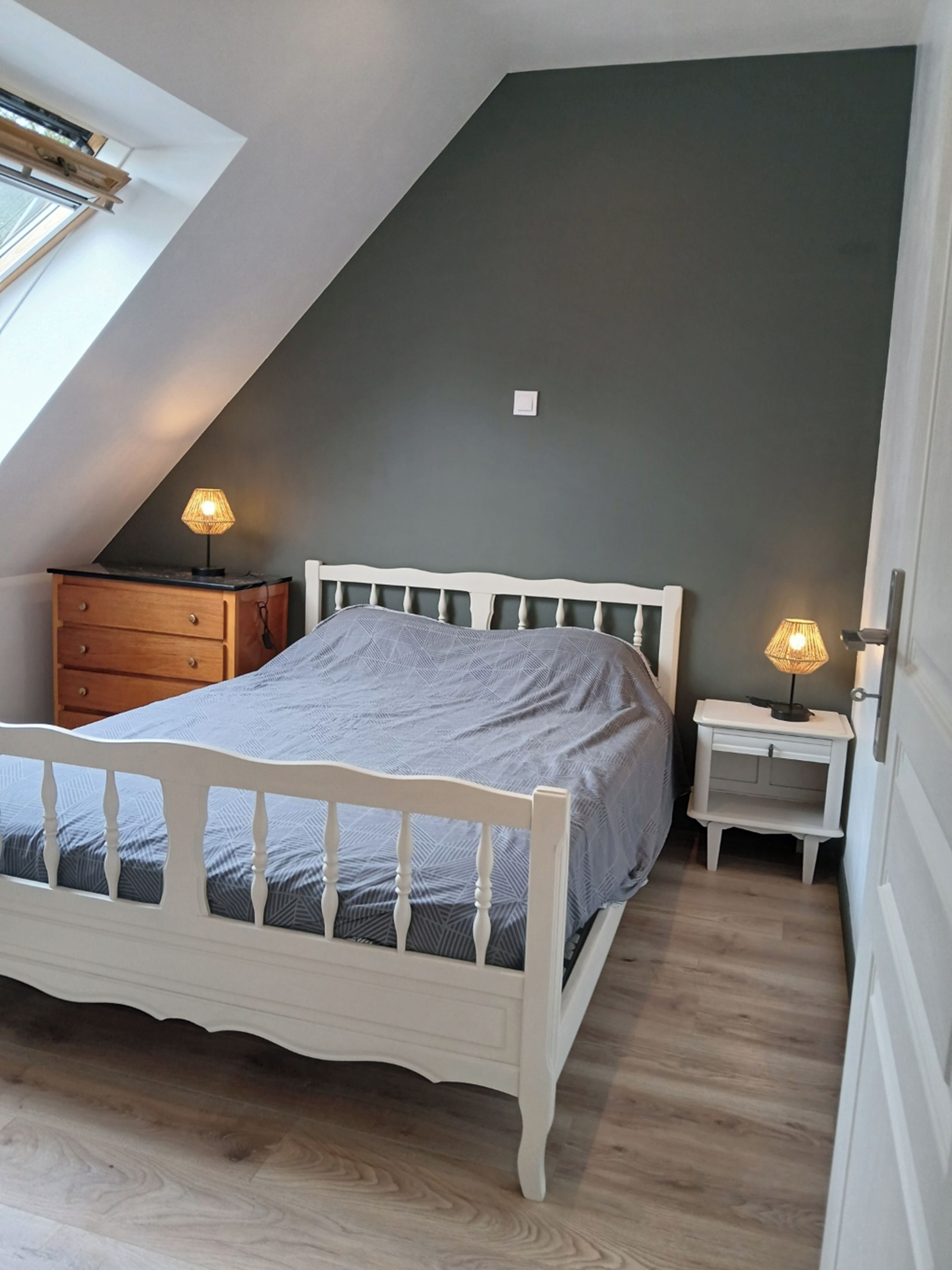 Une chambre à coucher avec un plafond en pente, un lit, deux tables de chevet avec des lampes et une commode.