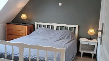 Une chambre à coucher avec un plafond en pente, un lit, deux tables de chevet avec des lampes et une commode.