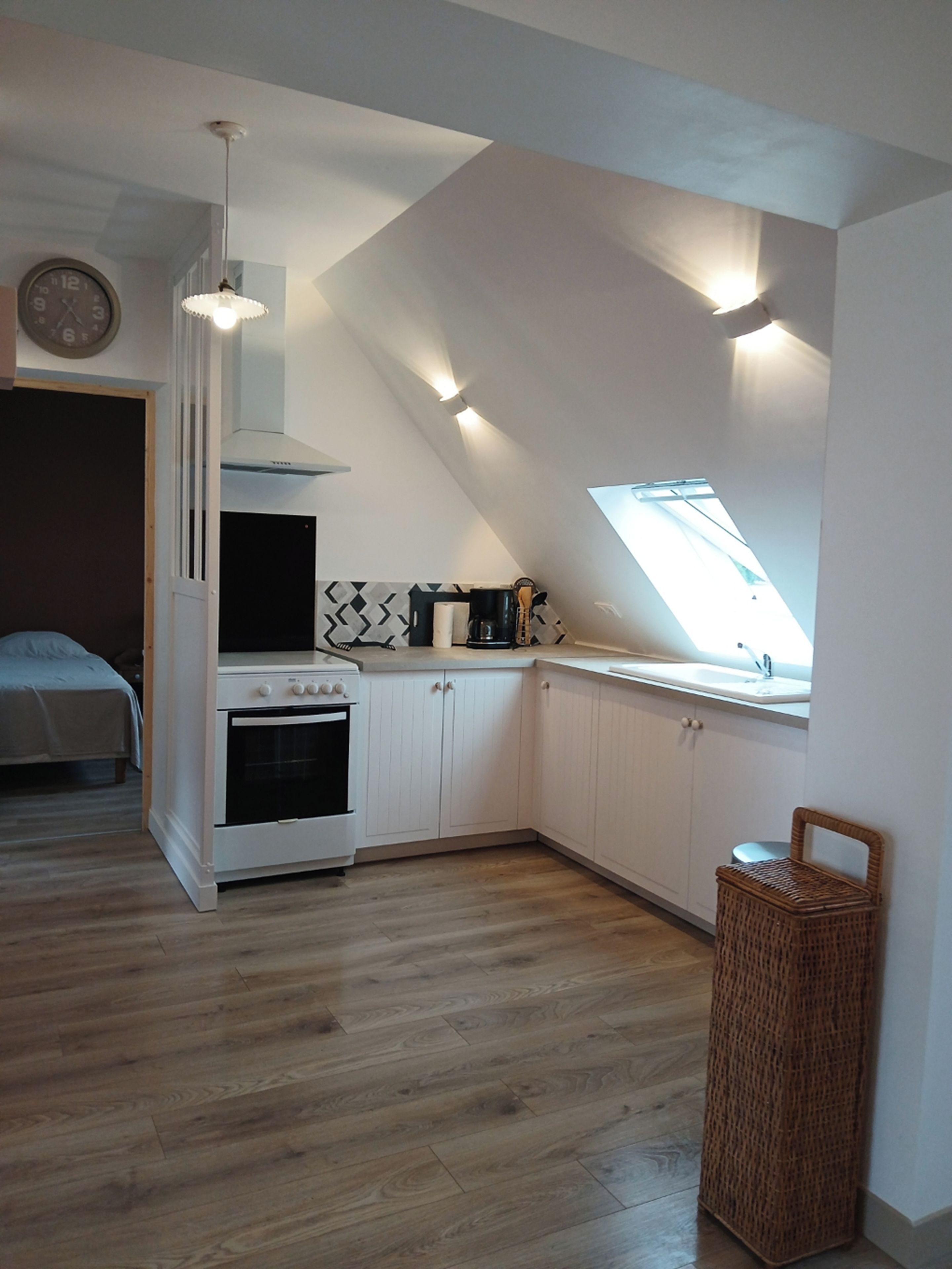 Een praktische keuken met een inbouwoven, witte kasten, een hanglamp en een dakraam.