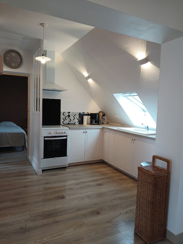 A compact kitchen with a built-in oven, white cabinets, a hanging light fixture, and a skylight.