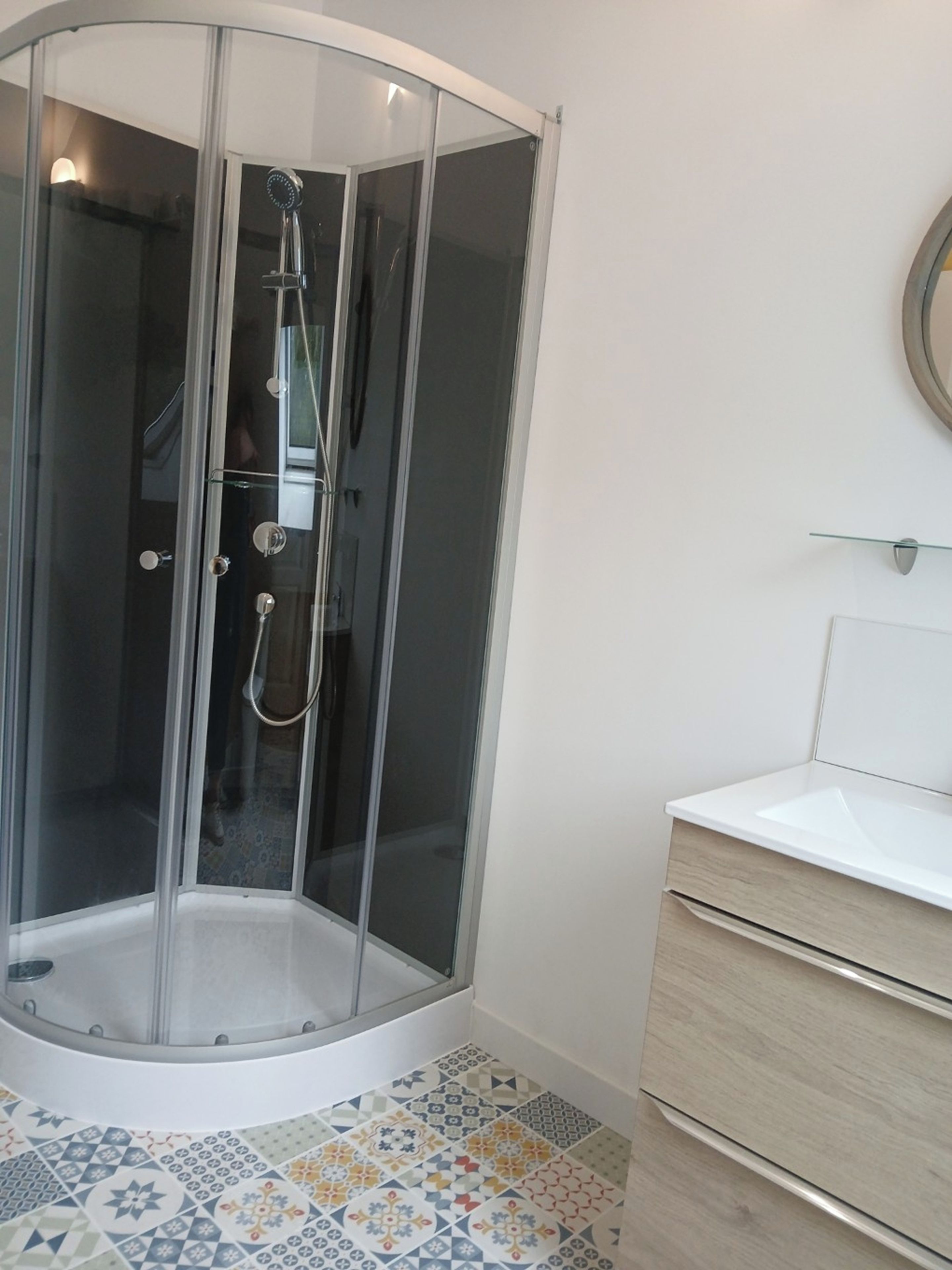 Une cabine de douche d’angle avec une porte en verre, un lavabo blanc et un sol carrelé.