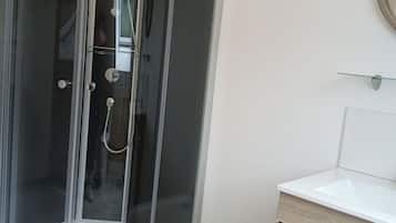 Une cabine de douche d’angle avec une porte en verre, un lavabo blanc et un sol carrelé.