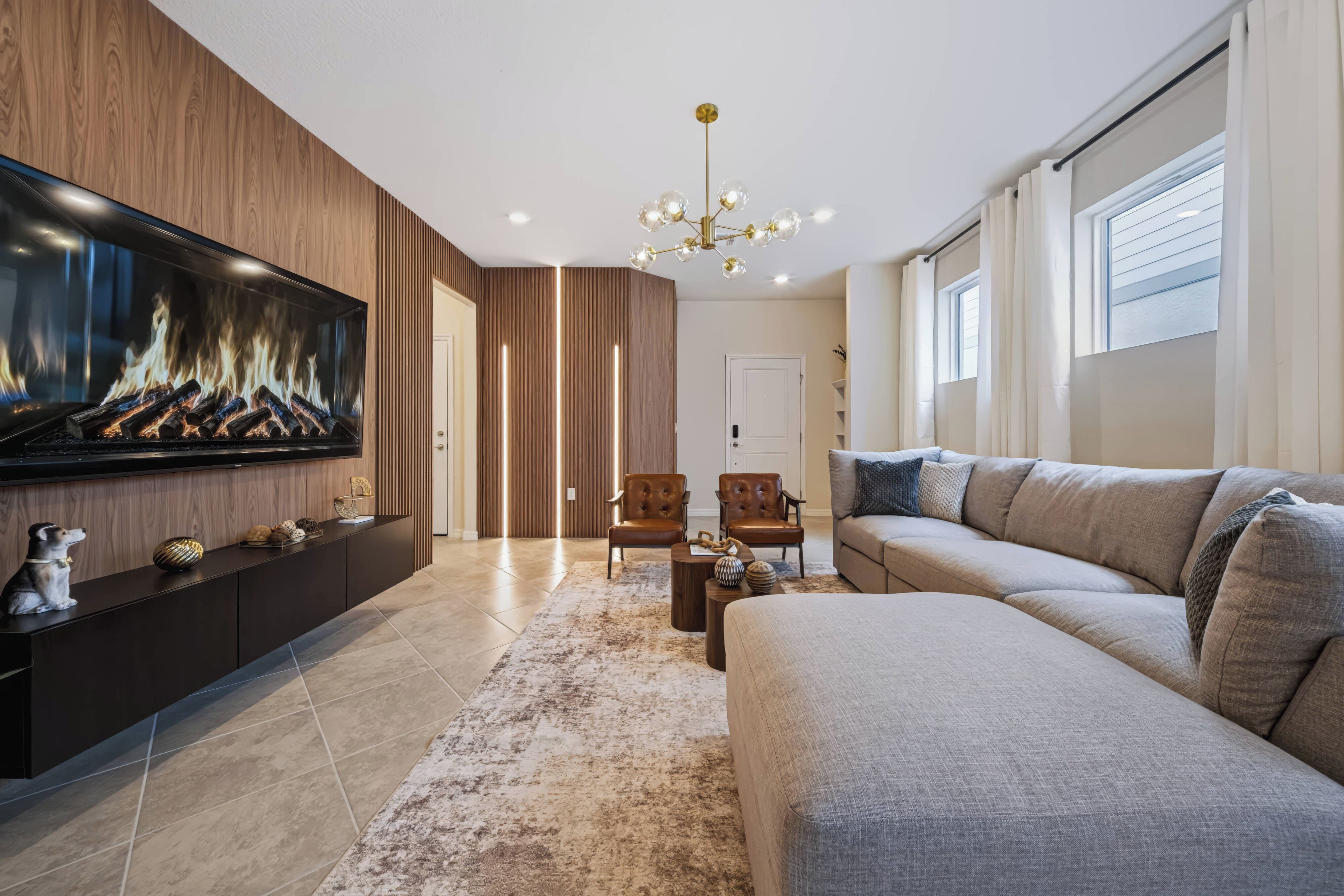 A modern living room with a flat-screen TV, leather sofas, a wooden accent wall, and a chandelier.