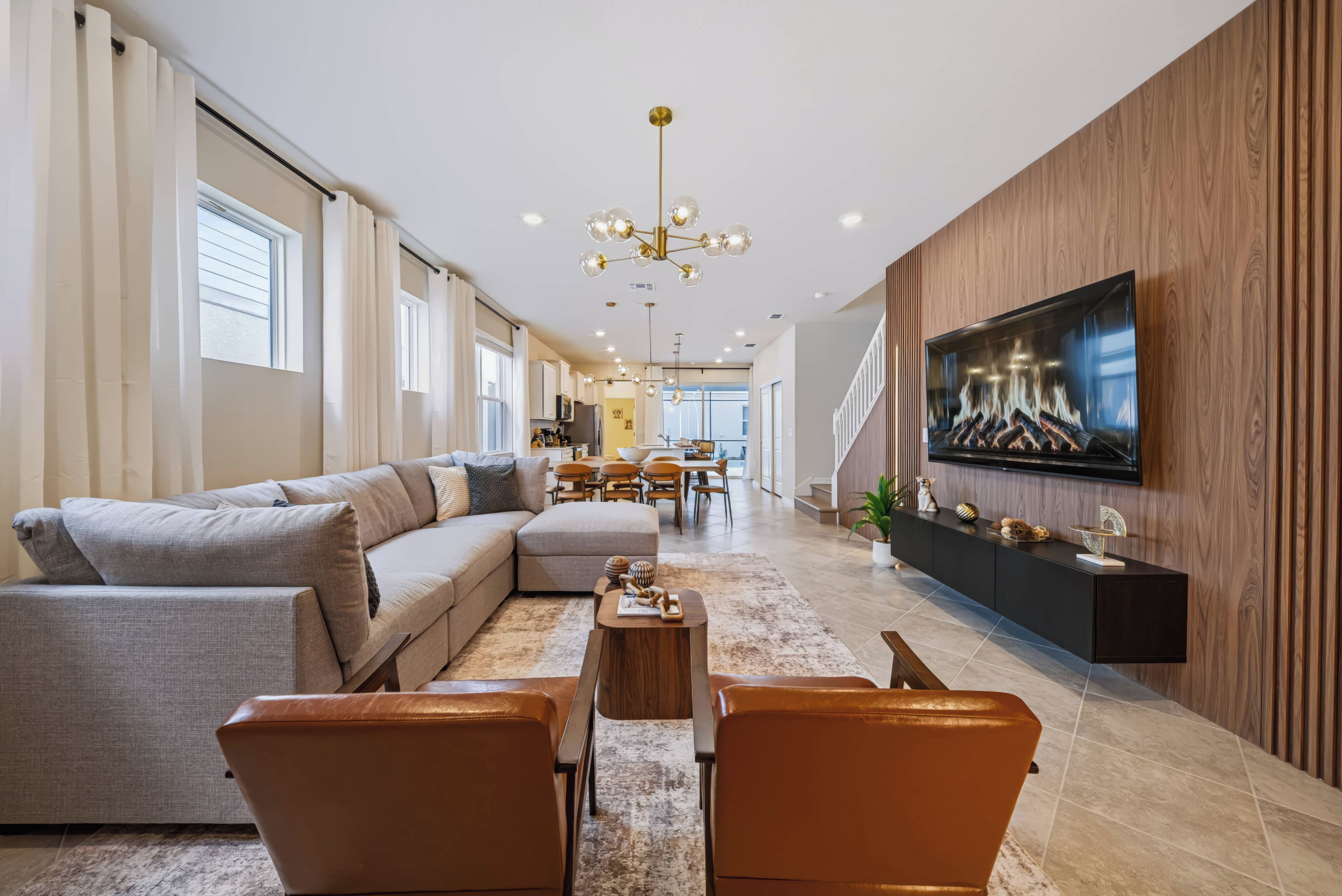 Un salon moderne avec un canapé d’angle, des fauteuils en cuir, une table basse et un téléviseur à écran plat fixé à un mur en bois.