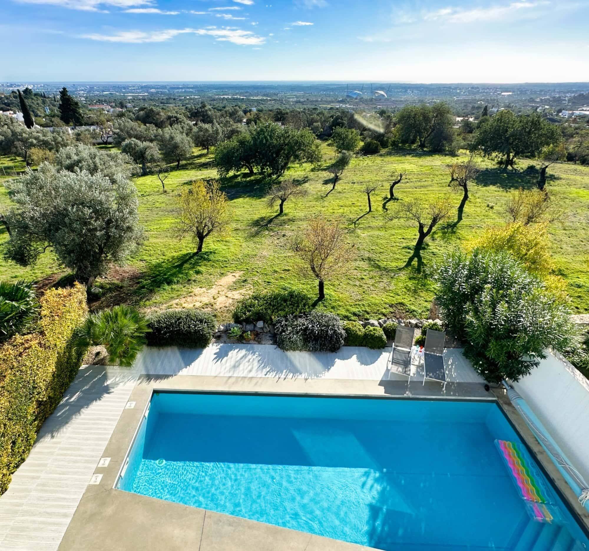 A swimming pool with a view of a vineyard and distant cityscape.
