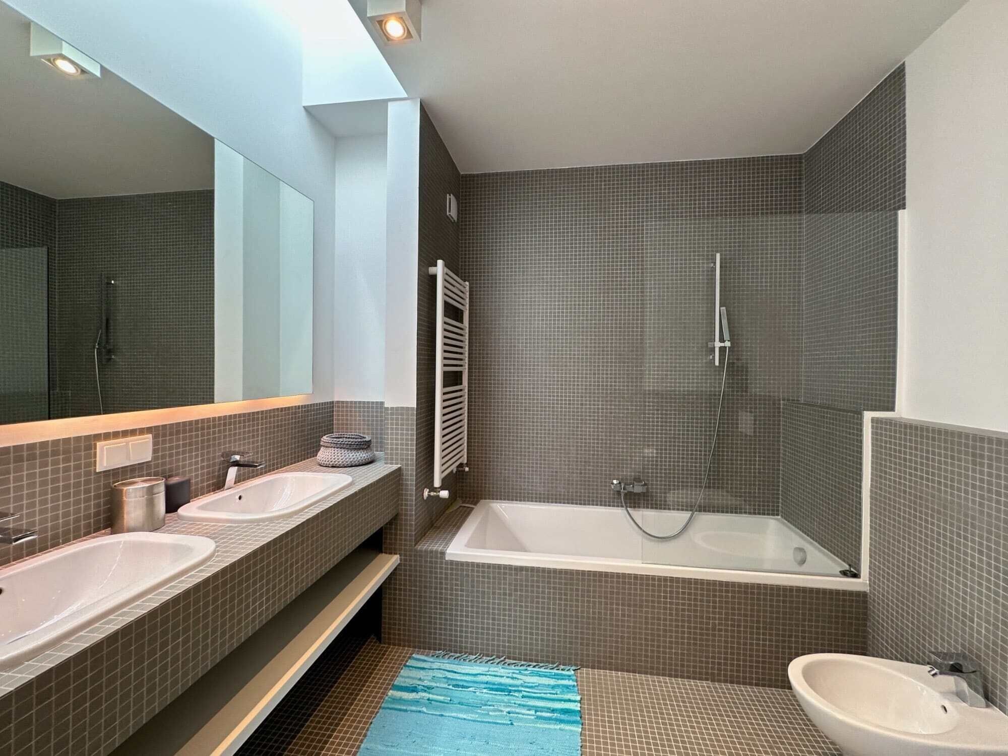 A modern bathroom with two sinks, a bathtub, and a shower.