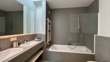 A modern bathroom with two sinks, a bathtub, and a shower.