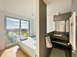 Un dormitorio con un ventanal que ofrece vistas de la ciudad, una cama con cabecera azul y vistas al exterior.