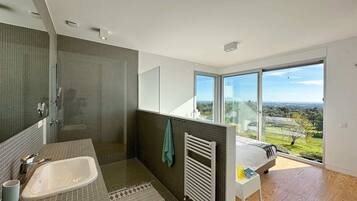 Un baño moderno con bañera, ducha y ventanas amplias que ofrecen vistas al exterior.