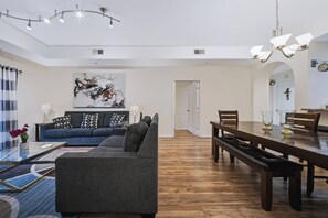 A modern living room with a sectional sofa, a dining table, and a chandelier. - Amazing 3BR at Caribbean Cove Resort Near Disney (Kissimmee)