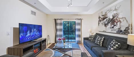 A modern living room with a flat-screen TV, a sofa, a coffee table, and a large abstract painting on the wall.