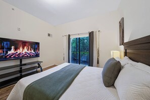 A hotel room with a bed, a television displaying a fire, a window with curtains, and a nightstand with a lamp. - Amazing 3BR at Caribbean Cove Resort Near Disney (Kissimmee)