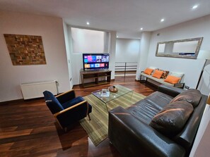 Ein modernes Wohnzimmer mit Sofa, Sessel, Fernseher und einer Wanddekoration.