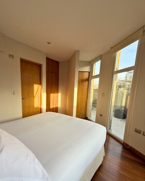 Ein Schlafzimmer mit einem großen Bett, Holztüren und einer Glastür, die zu einem Außenbereich führt.