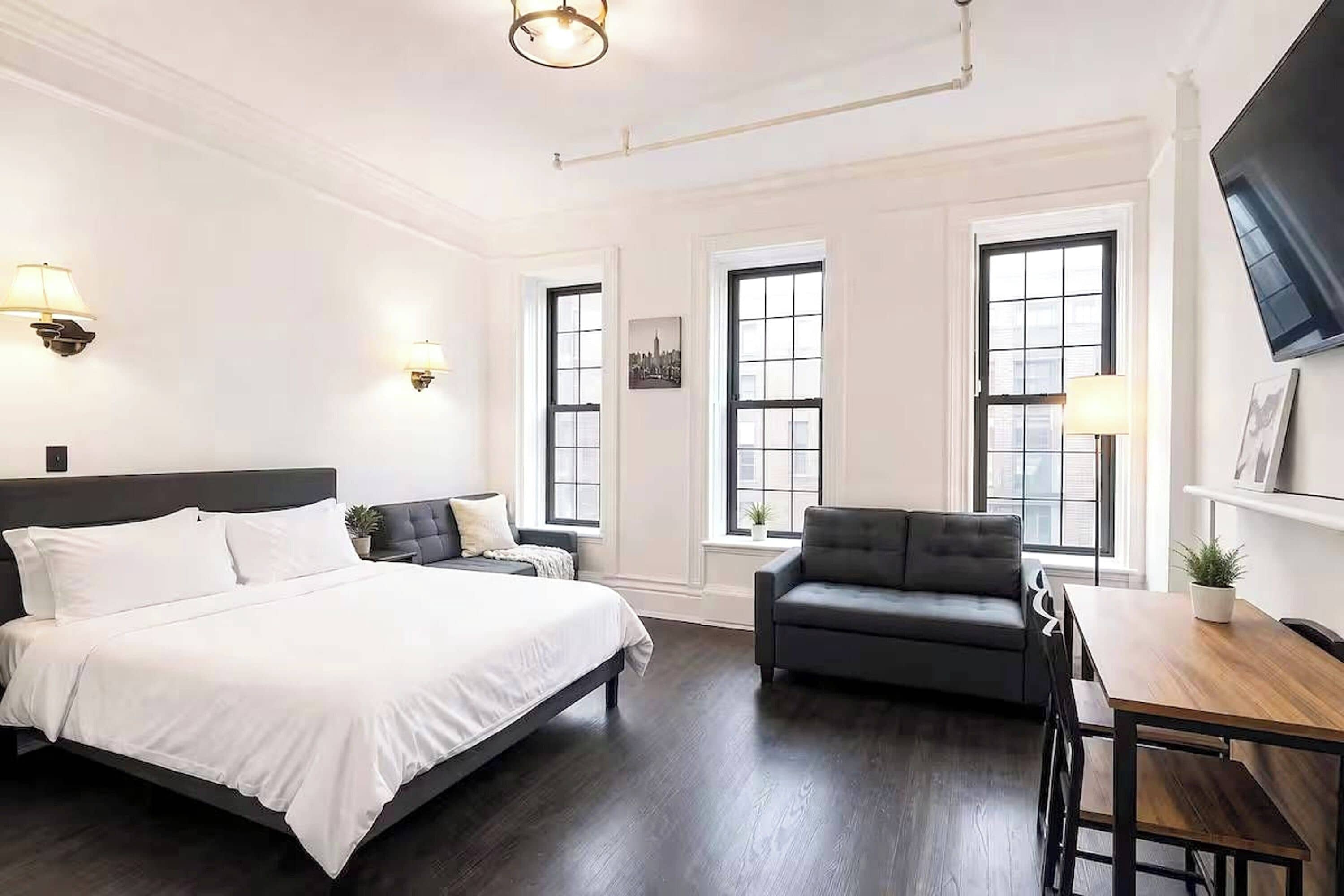 Habitación de hotel con una cama grande, un sofá, un escritorio y un televisor montado en la pared.