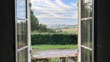 An open window with a view of a green landscape and a clear sky.