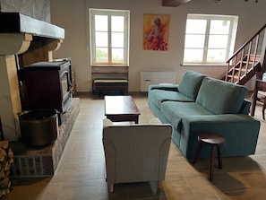 A living room with a sofa, a wooden table, a bench, a fireplace, and a painting on the wall. - Holiday Home 'La Colline' with Private Terrace, Wi-Fi and Air Conditioning (Lanty)