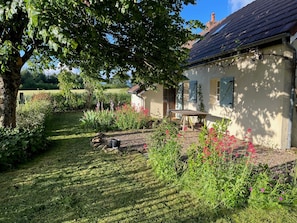 Een huis met een tuin, een bank en een boom.