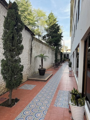 Un patio al aire libre con un camino empedrado, plantas en macetas y mobiliario exterior.