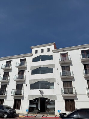 Un edificio de varios pisos con fachada blanca, múltiples balcones y entrada principal con puerta de cristal.