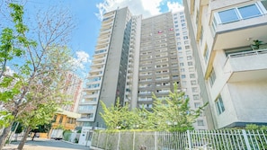 Un edificio residencial alto con varios balcones, entrada protegida y cielo despejado.
