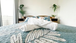Una cama bien hecha con cubrecama estampado con hojas, un cabecero de madera y dos mesitas de noche con plantas en macetas.